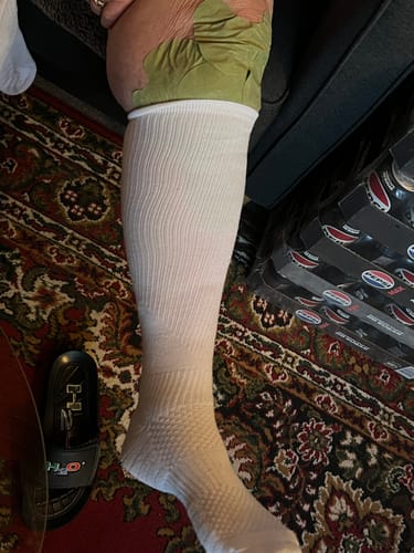 Anmelder der viser en hvid støttestrømpe på benet, mens personen sidder ned.