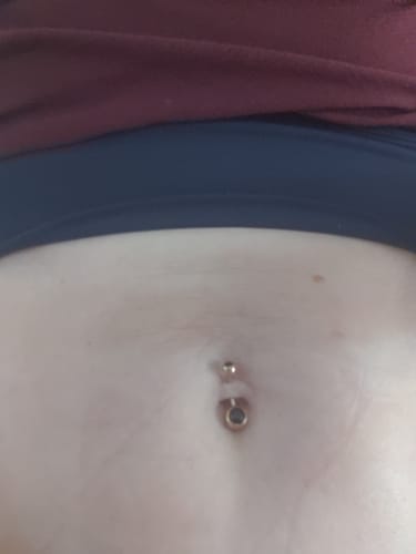 Close-up of a reviewer wearing the amethyst Classique Gem Belly Bar with rose gold plating in their navel.