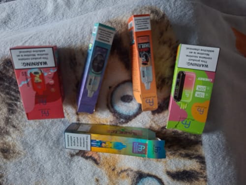 Kunde zeigt die farbenfrohen Verpackungen von fünf verschiedenen Vape-Produkten auf einer Decke.