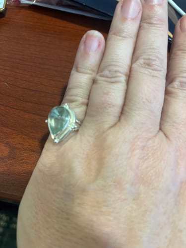 Reviewer's hand wearing the Teardrop Aquamarine Ring on their pinkie finger against a wooden surface.