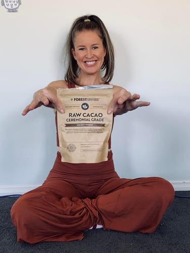 Reviewer smiling while sitting on the floor and holding up a bag of Raw Ceremonial Cacao.
