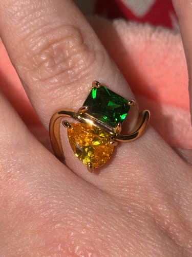 Customer wearing their Navae Birthstone Ring with a green radiant-cut stone and a yellow pear-cut stone on a gold band.
