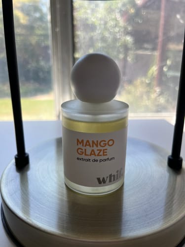 Customer's Mango Glaze perfume bottle with a round white cap, sitting on a metal stand.