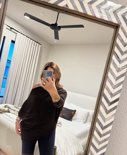 Reviewer in a mirror selfie wearing the espresso brown Asymmetric Draped top off one shoulder, showing the fit.
