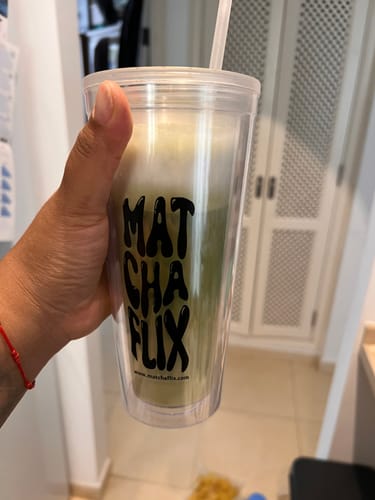 Un cliente sostiene un vaso transparente de Matchaflix con una bebida de té matcha espumosa.