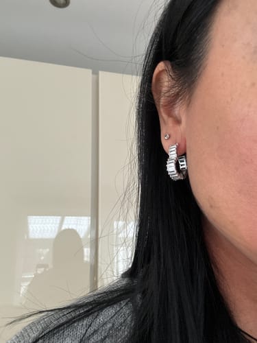 Nahaufnahme einer Kundin, die die silbernen Heart Hoops mit rechteckigen Steinen im Ohr trägt.