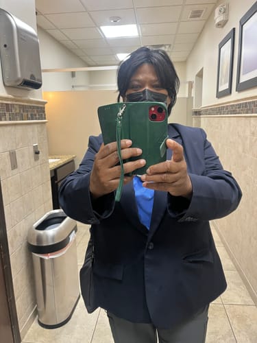 Reviewer wearing a short, jet black wig takes a mirror selfie in a public restroom.