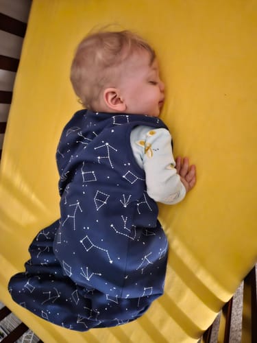 Customer's baby sleeps soundly in a crib wearing the dark blue Night Sky™ baby sleeping bag.