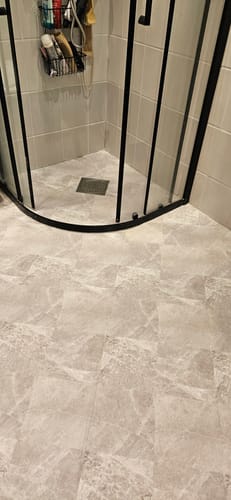 Kundes kalk beige selvklebende fliser lagt på et baderomsgulv foran en dusj.