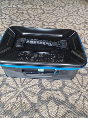 Klant toont de gesloten zwarte SUPERA X LARGE EVA ACCESSORY CASE met blauwe rand op een tapijt.