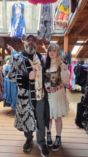 Reviewer wearing the 'Book of Dragons' shirt under a patterned coat with their daughter at a Renaissance Festival.
