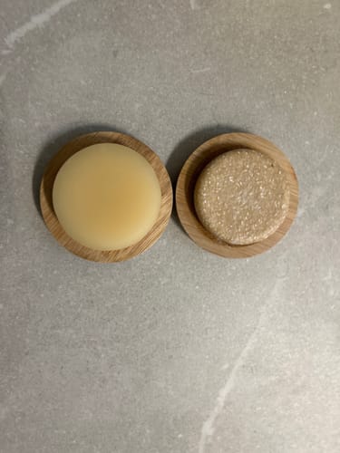 Customer's Ginger Shampoo Bar and conditioner bar resting on round bamboo drainers on a grey surface.