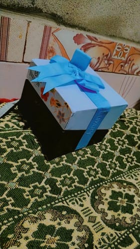 Customer's packaging for the Pearl Jewellery, a decorative box wrapped with a large blue ribbon on a patterned surface.