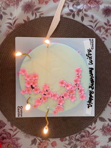 Reviewer's light blue Cherry Blossom Floral Cake decorated with pink flowers and lit birthday candles.