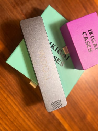 Customer's elegant metal pill case displayed on top of its mint green and magenta packaging boxes.