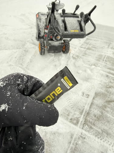 Customer's gloved hand holding a single packet of SuperCharged Honey in a snowy outdoor setting.