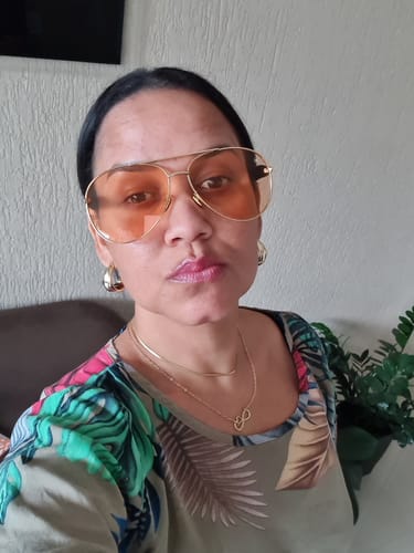 Cliente tirando uma selfie com os Óculos Savona, que possuem armação dourada e lentes laranja.