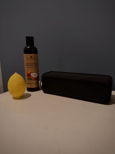 Customer's yellow Lem Clitoral Massager on a white surface next to a bottle of coconut oil and a black case.