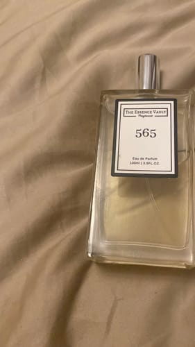 Customer's bottle of 565 perfume with its white label, resting on a rumpled beige fabric background.