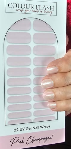 Eine Kundin hält die Verpackung der „Pink Champagne“ UV-Gel-Nagelfolien neben ihre kurzen, manikürten Nägel.