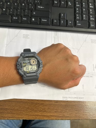 Cliente mostrando su reloj digital Casio Vintage WS-1700H en la muñeca, sobre un escritorio.