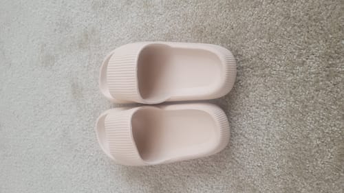A top-down view from a customer showing their pink Cloudies slippers on a gray carpet.