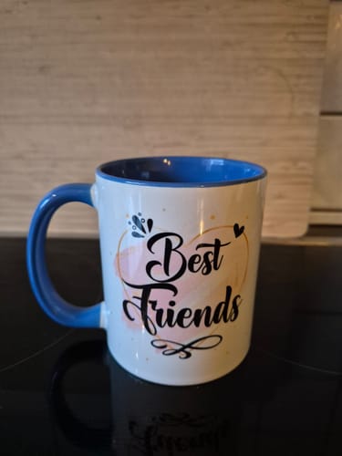 Kunde zeigt die bedruckte Tasse mit blauem Henkel und der Aufschrift 'Best Friends' auf der Vorderseite.