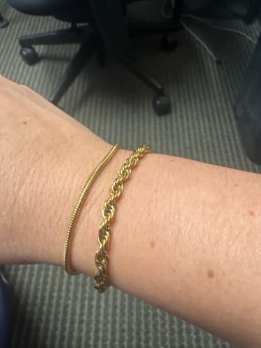 A reviewer shows a close-up of the gold Twisted Leila Layered Bracelet on their wrist.