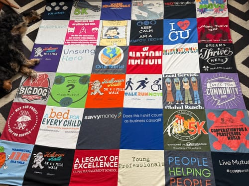 Reviewer's colorful Premium T Shirt Quilt made from professional event shirts spread out on a patterned rug.