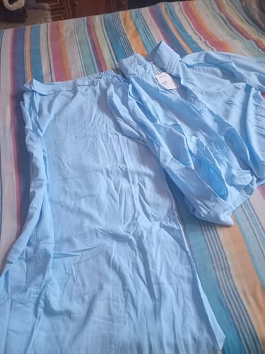 Customer's light blue top and skirt set laid out on a striped bedspread.