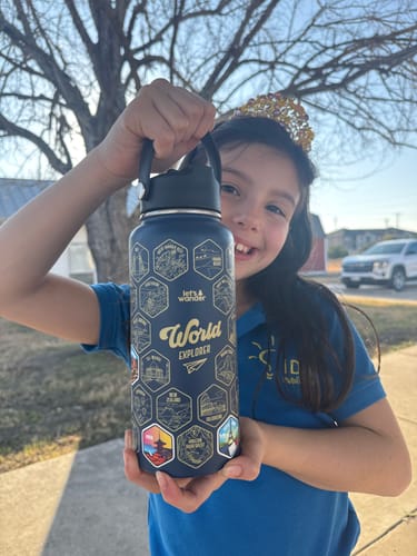 Customer holding their dark blue World Explorer Water Bottle with gold designs and colorful stickers applied.