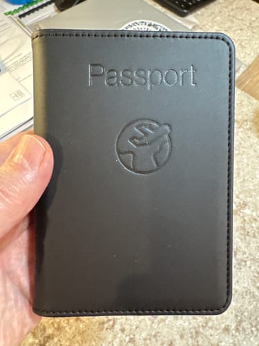 Customer holding the closed black Trackable Passport Cover, showing the embossed front.