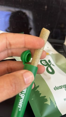 Customer's hand holding a Blue Dream pre-rolled joint next to its open green tube.