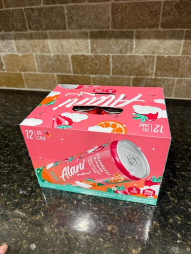 Customer's 12-pack box of Alani Nu Strawberry Sunrise energy drinks on a kitchen counter.
