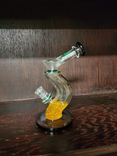 Customer's Hip Check Curved Glass Bong with its unique S-curve design, shown on a dark wood shelf.