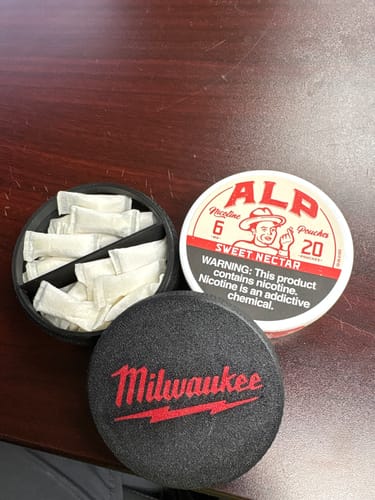 Reviewer's can of Sweet Nectar Nicotine Pouches next to an open black case showing the white pouches.