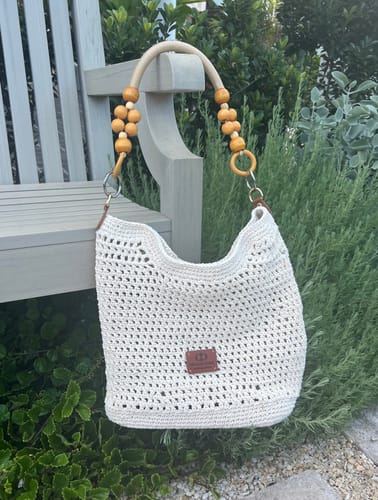 Reviewer's completed cream Sunny Beach Tote with a beaded handle, hanging on a wooden bench outdoors.