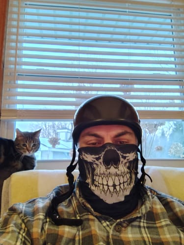 Reviewer wearing the Reaper Grin Skull Neck Gaiter and a helmet indoors in front of a window.