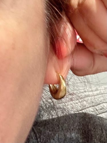 Close-up of a reviewer wearing a gold Mini Drop Huggie earring, highlighting its small size on the earlobe.