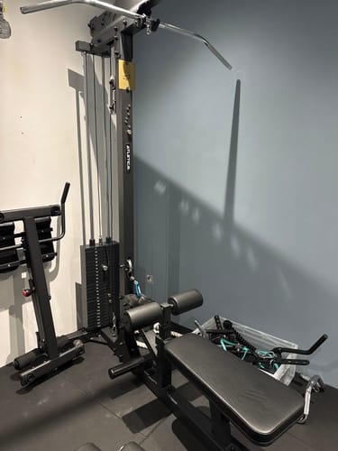 Rezensent zeigt die aufgebaute, schwarze Latzug mit Ruder-Station in einem Home-Gym.