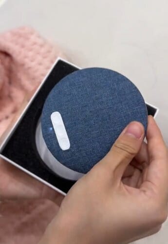 Customer holding the round, blue fabric Litlamp Pillow Speaker, taking it from its box.