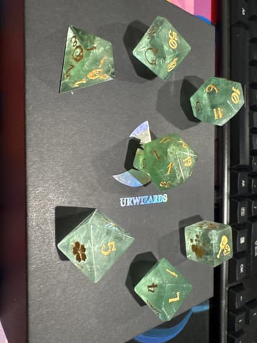 Customer's green fluorite dice set arranged on a black surface. The translucent dice have gold numbers and custom symbols.