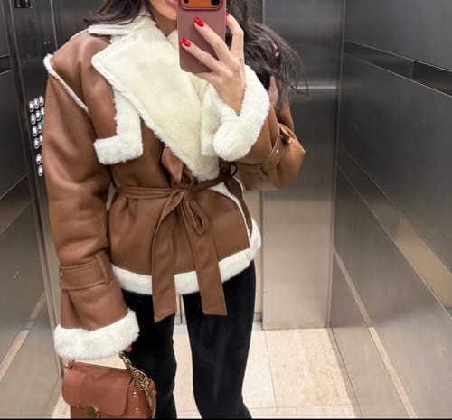 Customer taking a mirror selfie in the brown Vegan Leather Sherpa Coat, styled with black leggings.