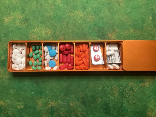 Customer's orange metal pill case, open with seven compartments filled with various sorted pills and vitamins.