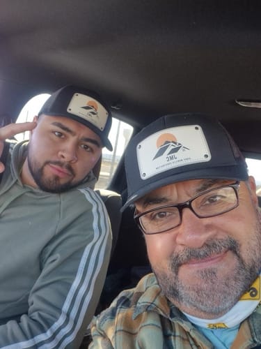 Two customers wearing matching black Image Hat Rectangle hats with custom mountain logo patches inside a car.