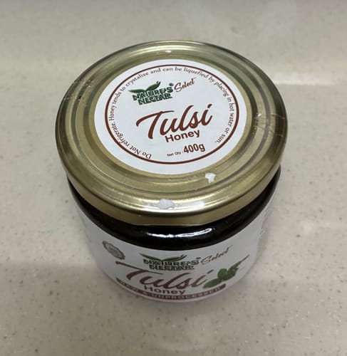 Reviewer's sealed 400g glass jar of dark Raw Tulsi Honey on a countertop.