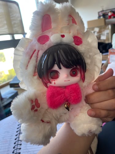 Customer holding a white ANTOO Paradise Lost Series plush toy with a doll face and bright pink bow.