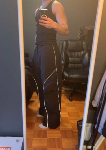 Reviewer's mirror selfie of the Black Retro Track Snow Pants, showing the baggy fit, reflective piping, and slightly short length.