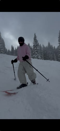 Reviewer wearing the baggy beige snow pants while skiing on a snowy slope.