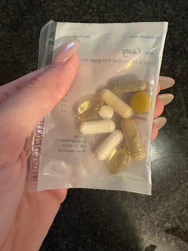 Customer holding a daily packet of assorted vitamin pills, including Biotin.